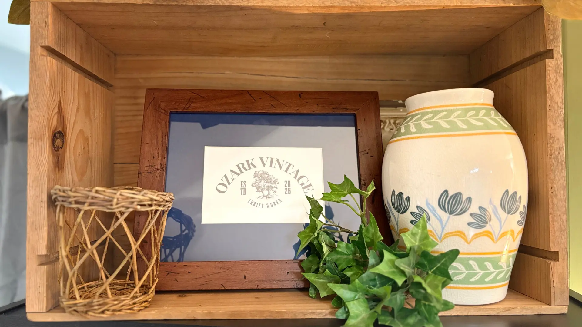 Curated Ozark Vintage Thrift Works shelf display with logo, woven basket, and hand-painted vase
